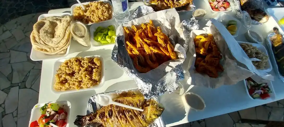 An overhead shot of a white table laden with a lavish spread of Middle Eastern or Mediterranean food, including grilled…