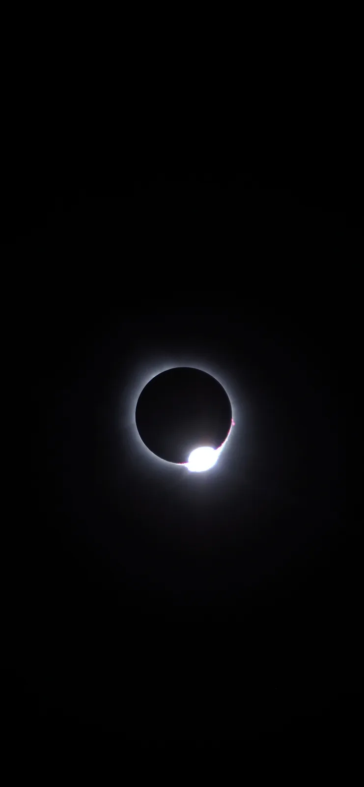 A photograph of a solar eclipse where the moon obscures most of the sun, leaving a bright crescent and a glowing corona…