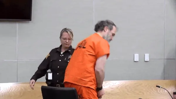 A man in an orange jail jumpsuit is shown in a courtroom, initially standing then slowly reclining in his chair as a…