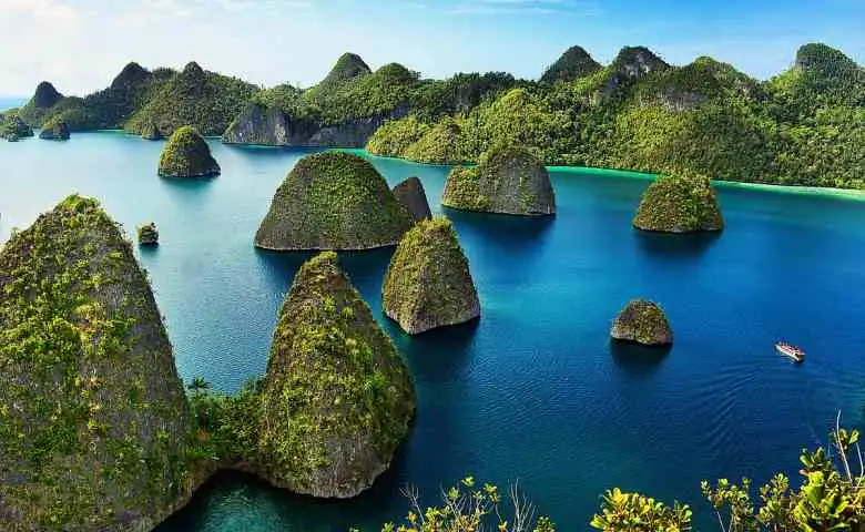A scenic photo of a tropical bay with numerous green, cone-shaped limestone islands rising from deep blue water, with a…