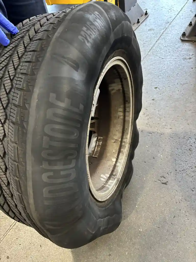 A close-up photo shows a large, dirty Bridgestone tire on a concrete floor, with a person's gloved hand visible near the…