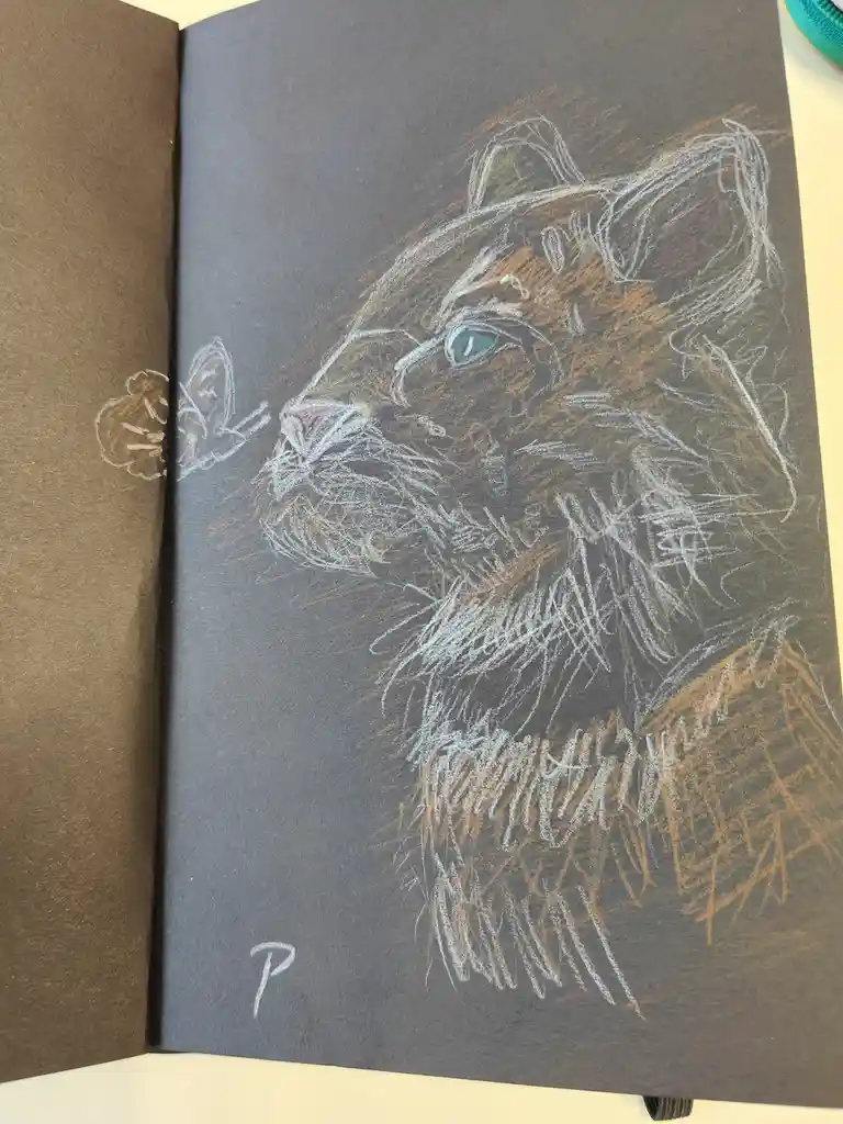 A sketchbook page shows a detailed colored drawing of a cat's head and shoulders, rendered in chalk or pastel on dark paper…