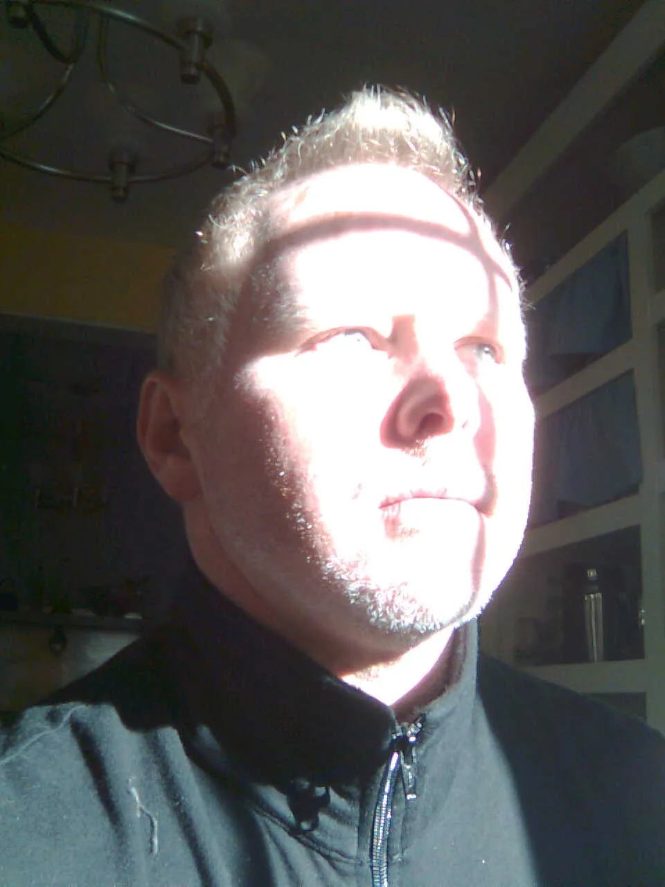 A man with short, light-colored hair and a goatee looks upward with a slightly squinting expression, his face partially…