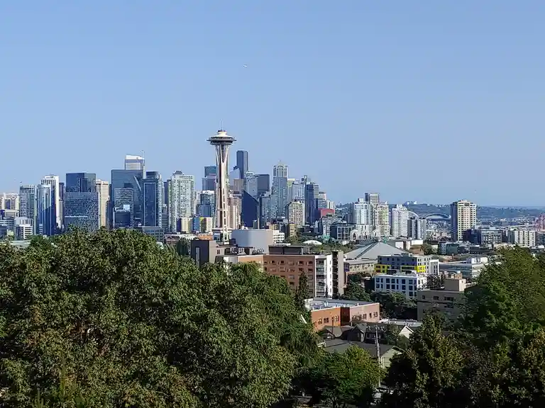 A clear daytime photo of the Seattle skyline, prominently featuring the Space Needle, surrounded by modern skyscrapers and…