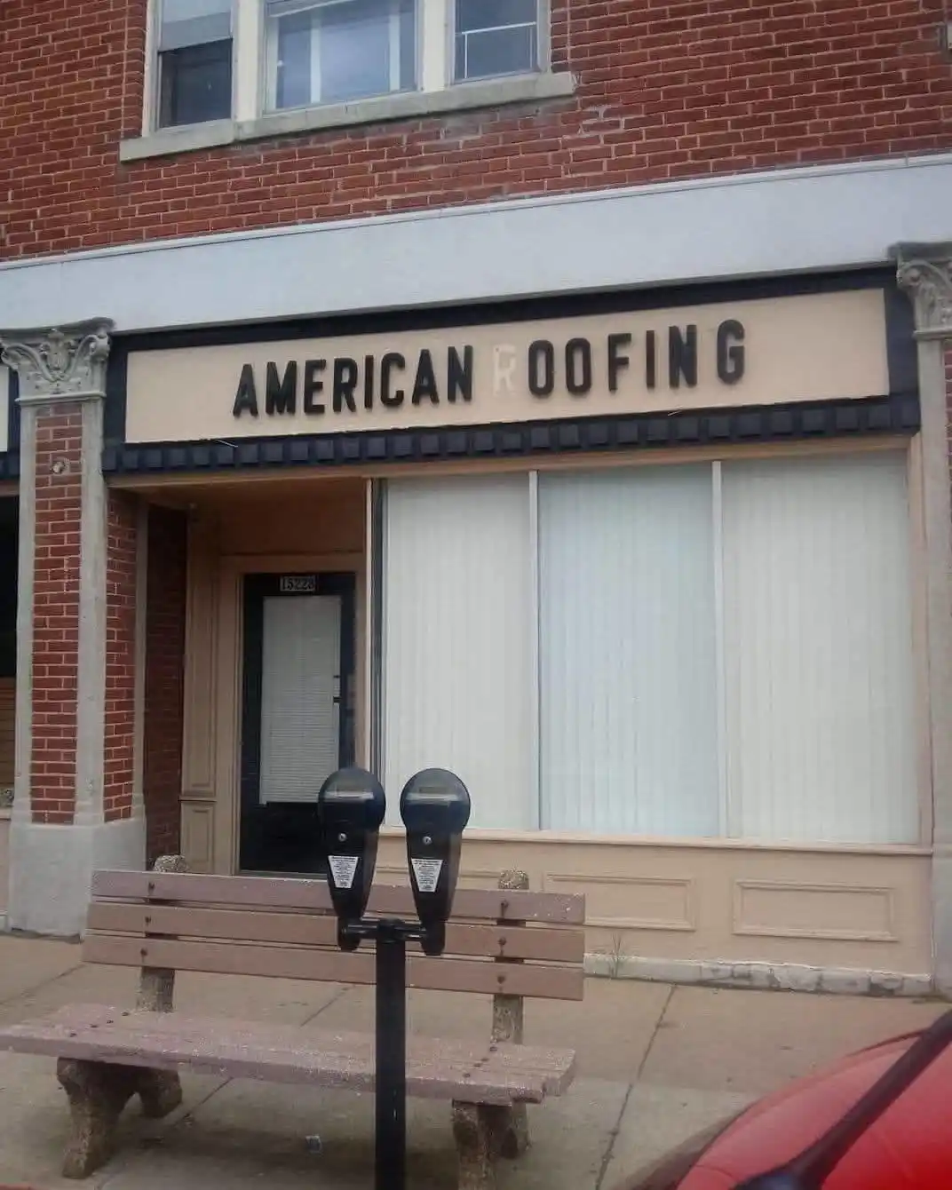 A storefront with a sign reading 'AMERICAN ROOFING' where the letter 'O' is replaced with a white, blank space. In front, a…
