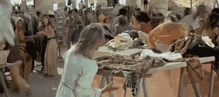 A sequence of six frames from a film depicting a person in a white robe moving through a crowded marketplace filled with…