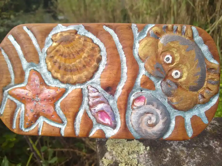 A hand-painted wooden plaque features stylized sea life including a starfish, scallop shell, conch shell, and a cartoonish…