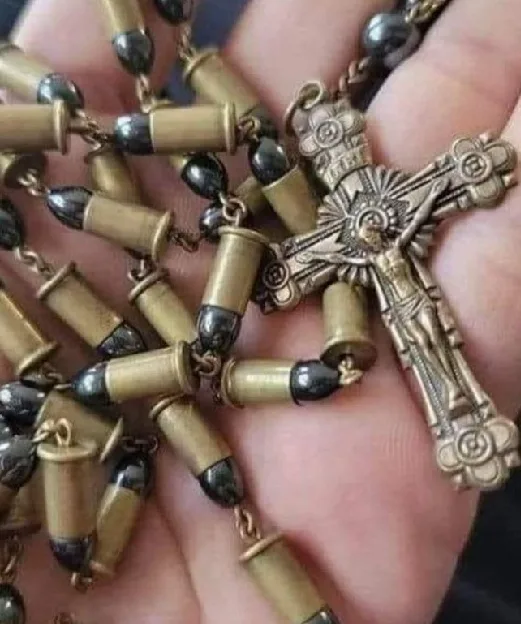 A close-up image shows a hand holding a rosary where the traditional beads are replaced with brass-cased bullets, and the…