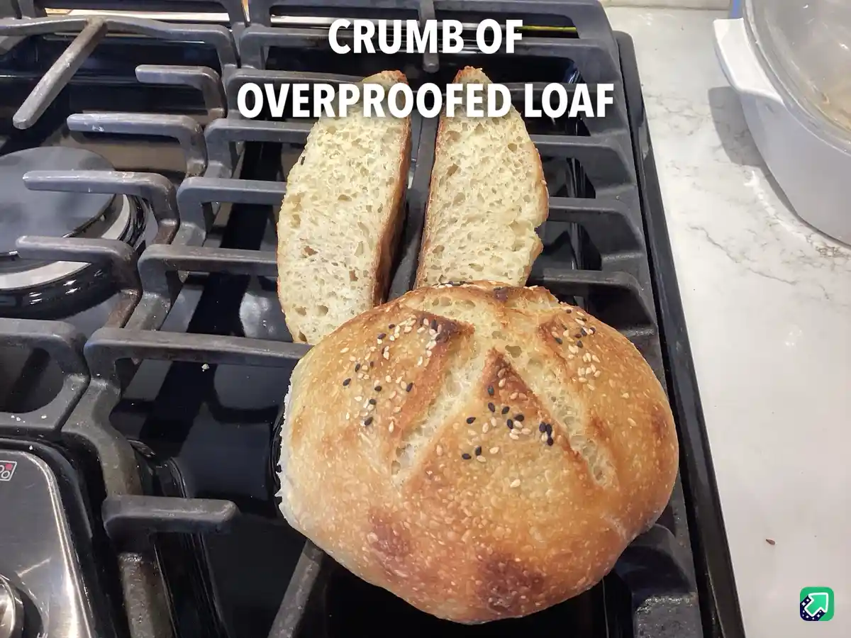 A round, golden-brown bread loaf with sesame seeds sits on a black gas stove burner, with two slices standing upright behind…