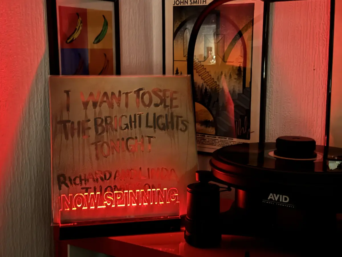 A red-lit sign in front of a record player reads 'I WANT TO SEE THE BRIGHT LIGHTS TONIGHT RICHARD AND LINDA THOMPSON NOW…