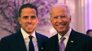 A photo of two men in suits smiling at the camera, one with dark hair and the other with white hair. The image has text…