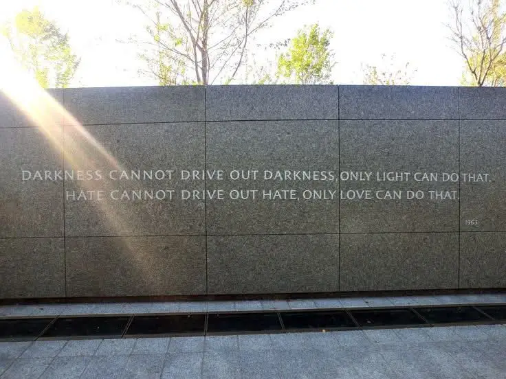 A photo of a granite memorial wall engraved with the quote 'DARKNESS CANNOT DRIVE OUT DARKNESS ONLY LIGHT CAN DO THAT. HATE…