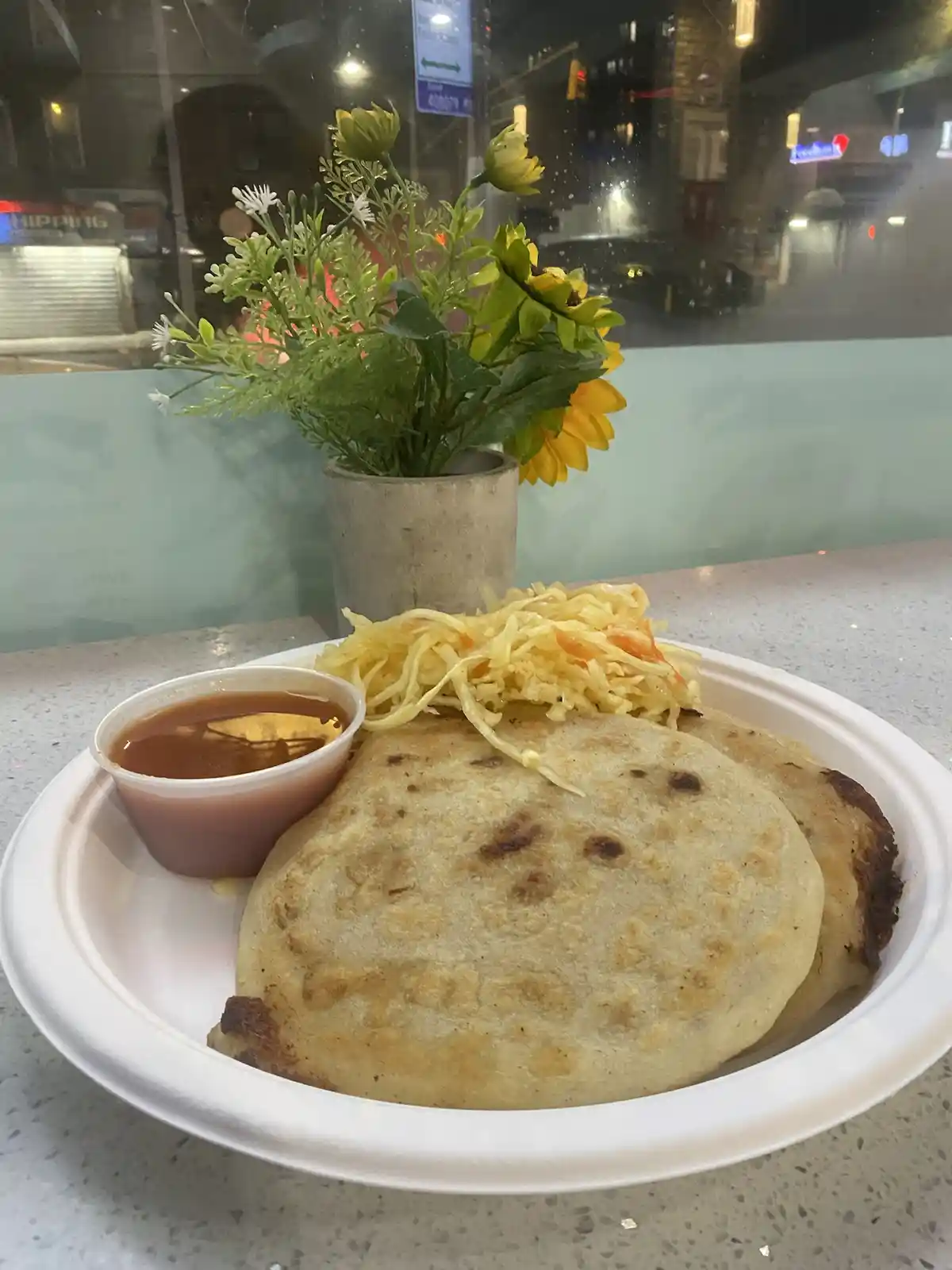 A white paper plate holds two golden-brown, slightly charred roti flatbreads with shredded yellow and orange vegetable salad…