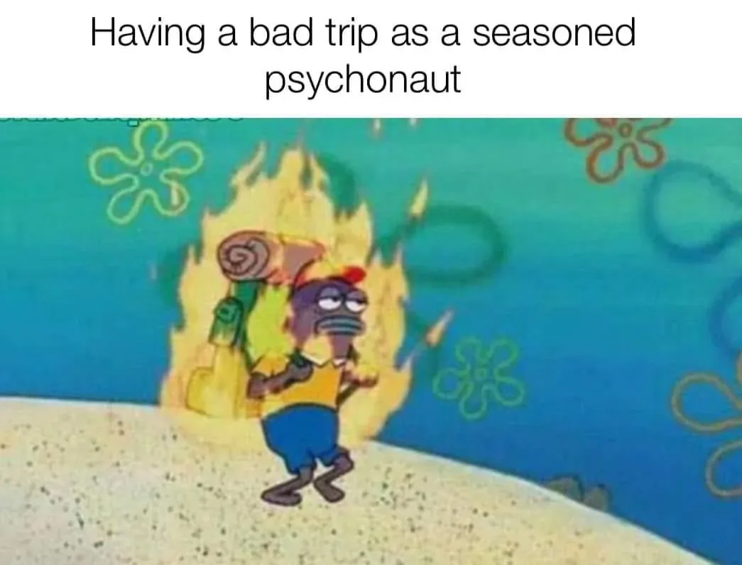 A cartoon character, resembling SpongeBob SquarePants with a purple face and tired expression, is engulfed in flames while…