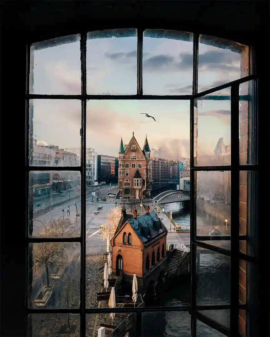 A view from inside a building looking out through a large, multi-paned arched window at a cityscape featuring a prominent…