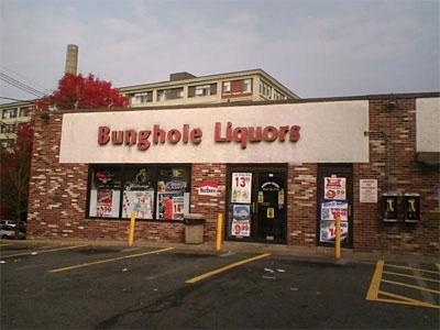 An exterior shot of a brick building with a large sign reading 'Bunghole Liquors' in red letters. The storefront has windows…