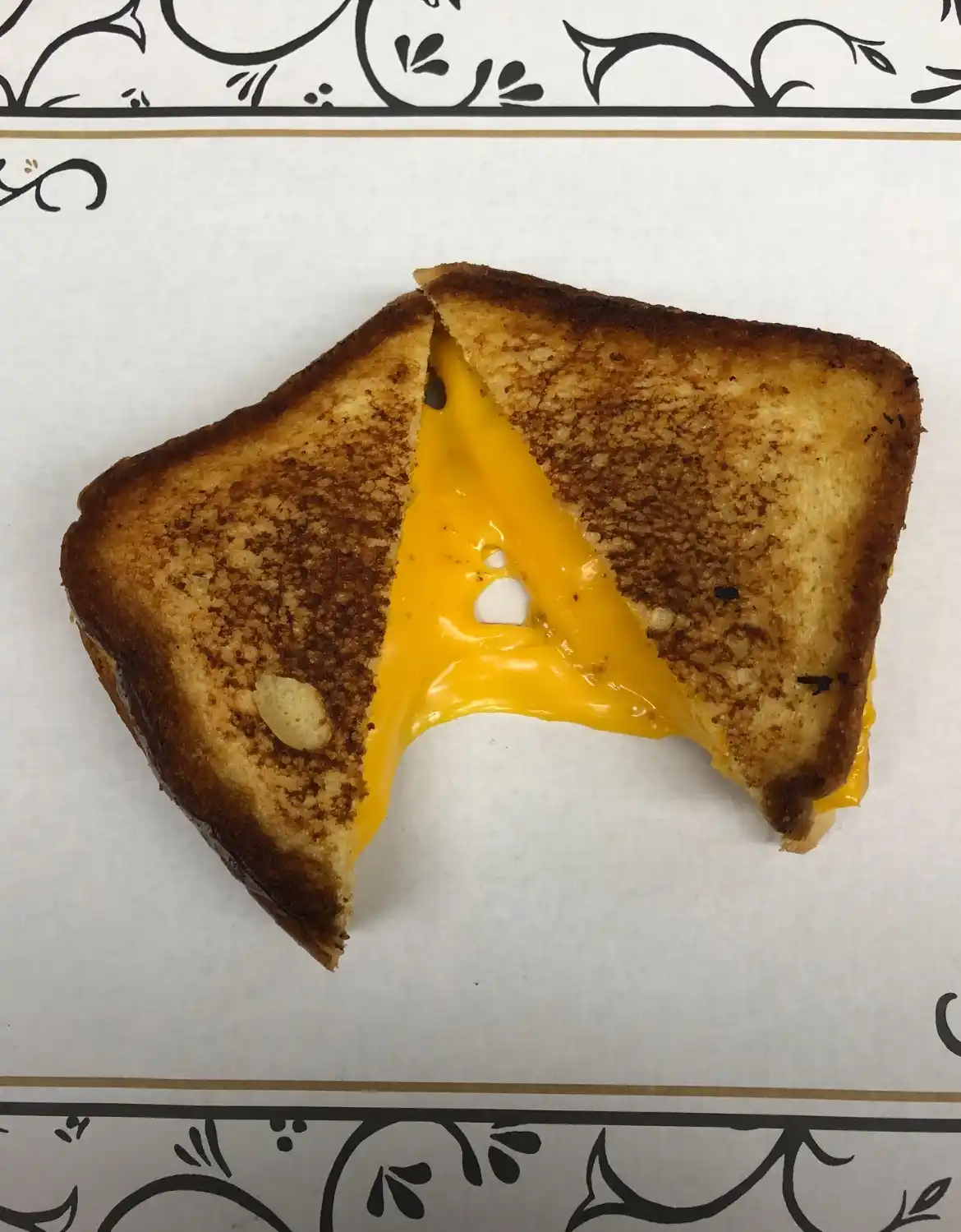 A perfectly toasted grilled cheese sandwich, cut diagonally in half, reveals a generous amount of melted, gooey yellow…
