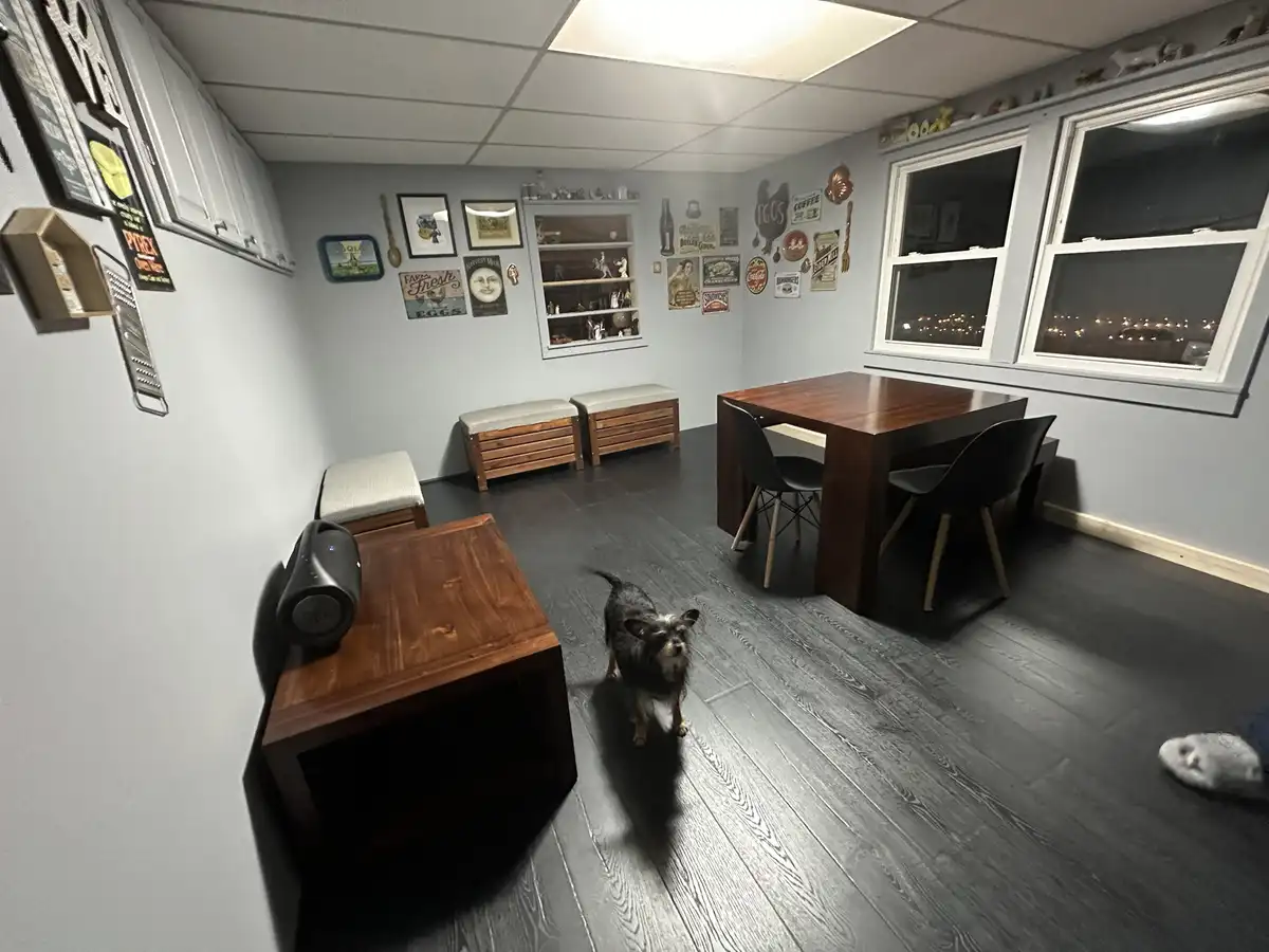 A wide-angle shot of a tidy, modern dining room with dark wood floors, a wooden table with black chairs, and a small…