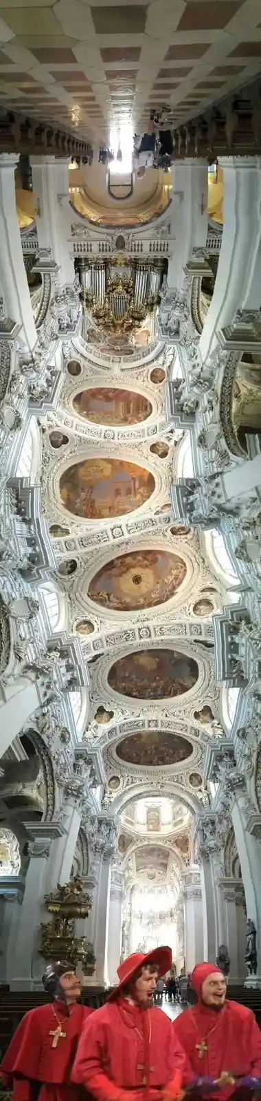 The image shows a vertically flipped photo of the ornate interior of a grand baroque cathedral, with its ceiling and…