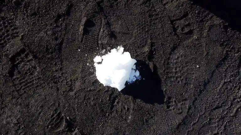 A small, bright white snowball rests on a dark, textured surface that appears to be black sand or volcanic soil. The…