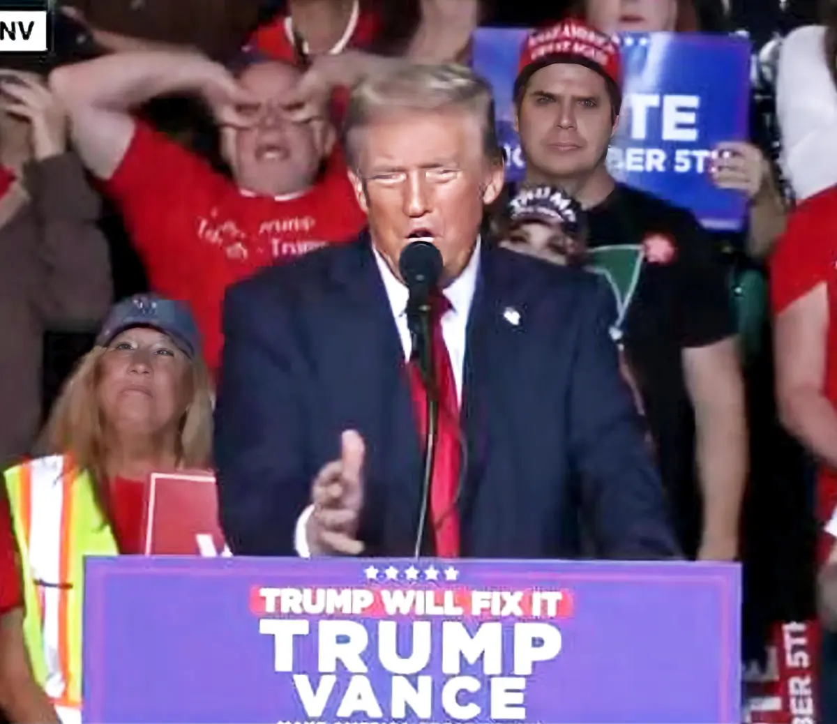 A photo of Donald Trump speaking at a rally with a purple podium that reads 'TRUMP WILL FIX IT TRUMP VANCE'. Behind him, a…
