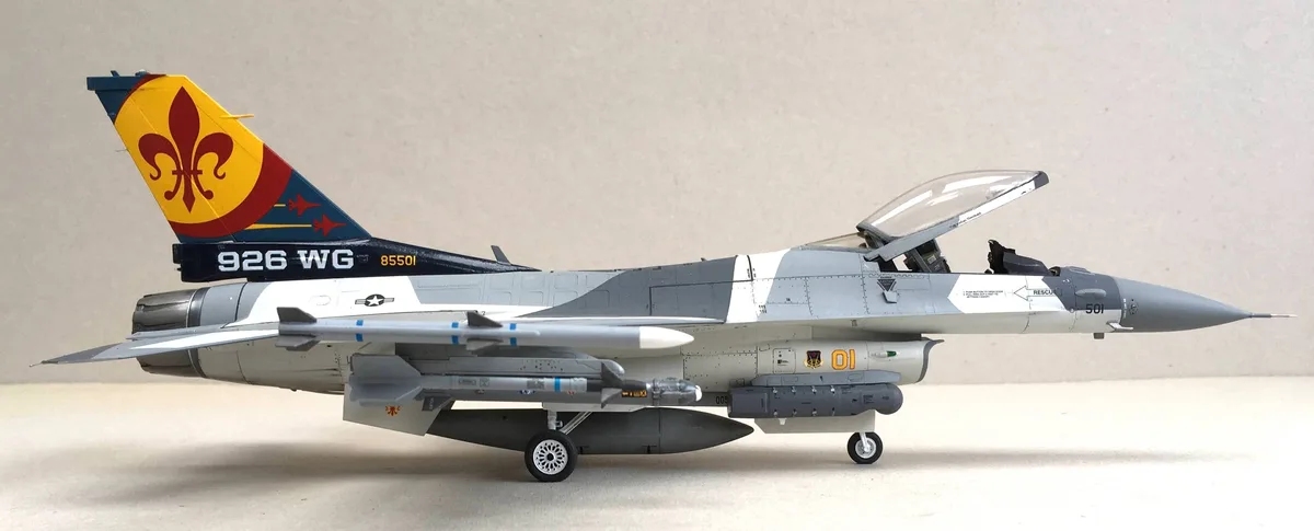 A detailed scale model of a gray military jet fighter with its canopy open, mounted with various missiles and bombs under…