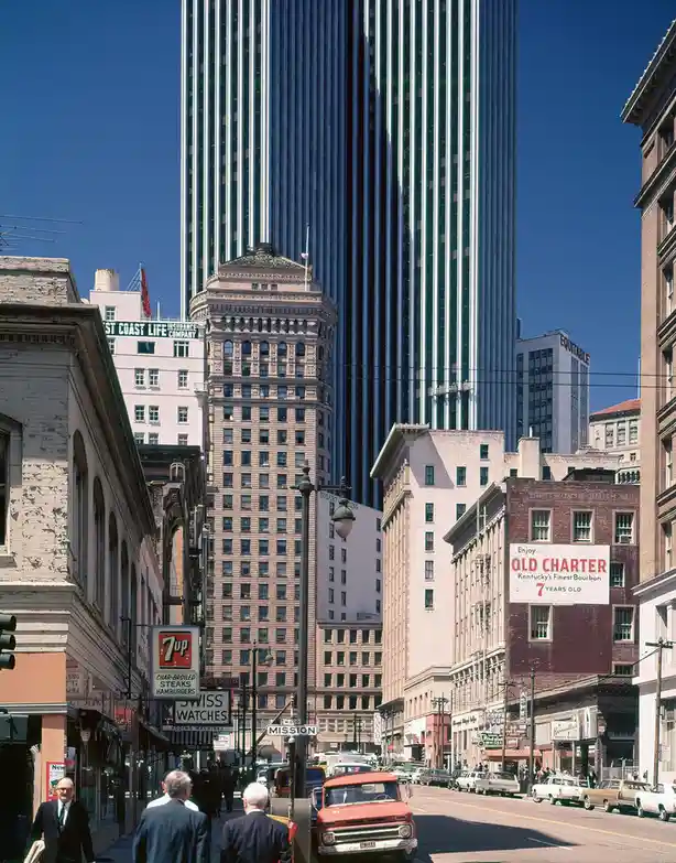 A vintage photograph of a bustling city street with a mix of old and new architecture, including a prominent striped…