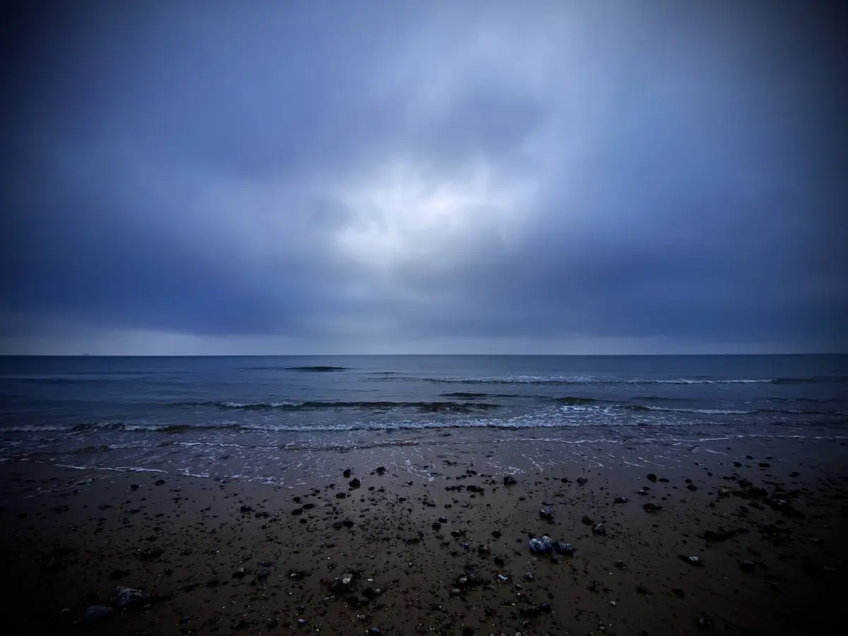 A moody, dark beach scene with a cloudy sky and waves rolling onto a pebbly shore. The overlaid text reads 'i'm not crying…