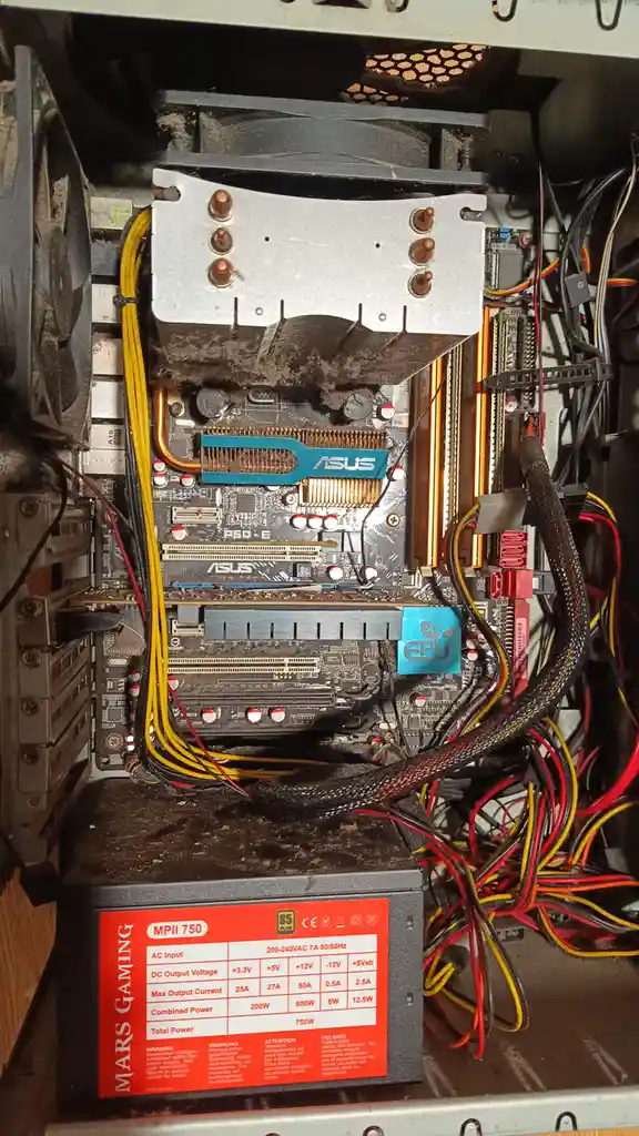 The image shows the inside of a heavily dust-covered and messy computer case, featuring an ASUS motherboard, a large CPU…