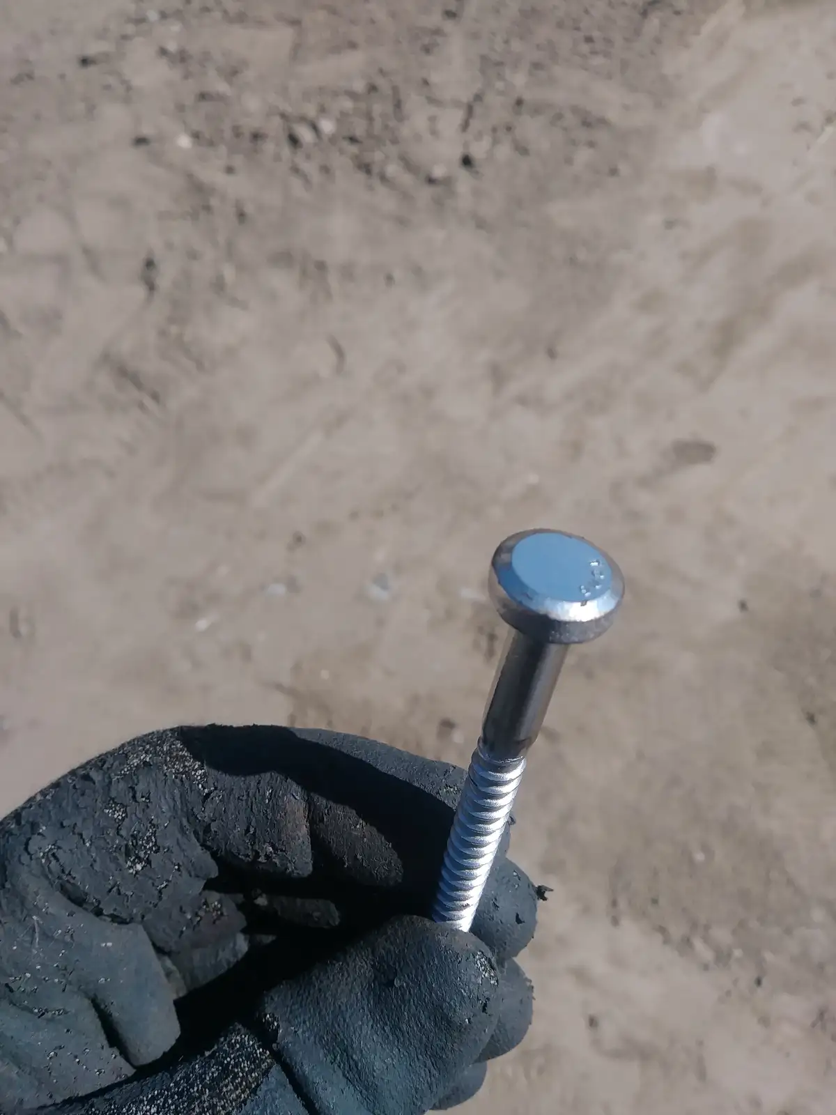 A gloved hand holds a metal bolt with a blue-tinted head against a sandy background. The overlaid text reads 'i found a bolt…