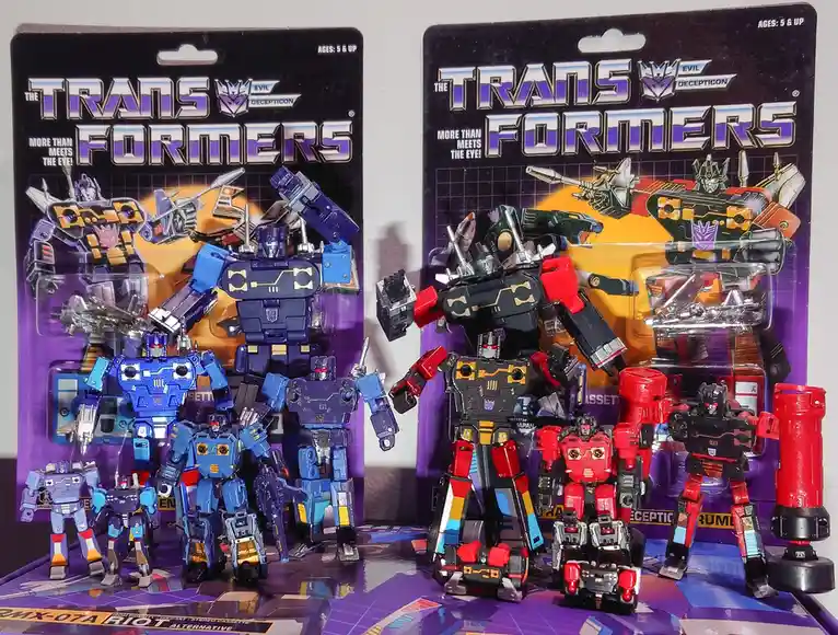 Two Transformers toy packages, one blue and one red, are displayed with their respective figures taken out and arranged in…