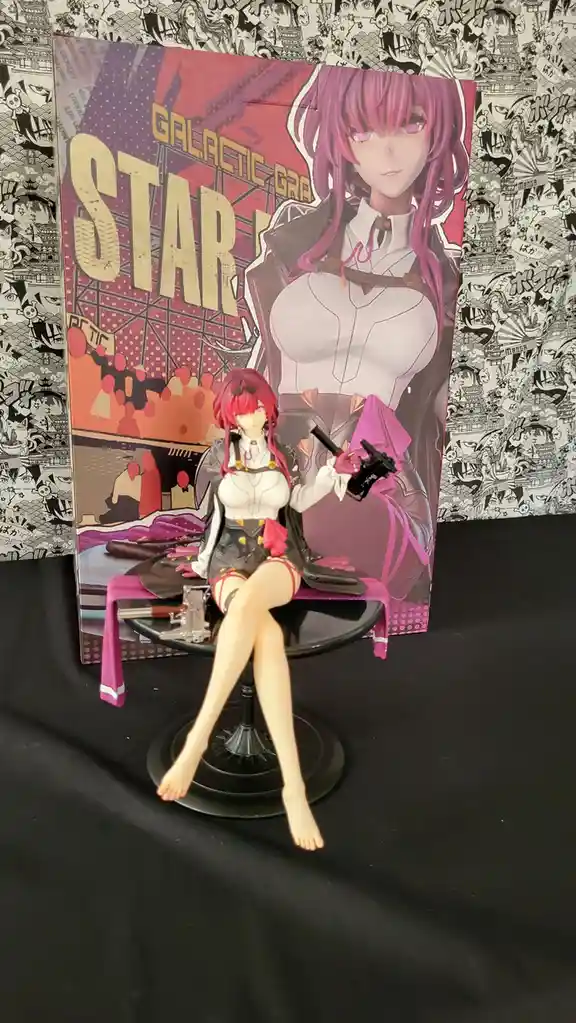 A detailed anime-style figurine of a woman with pink hair, wearing a white and black outfit with red accents, sits barefoot…