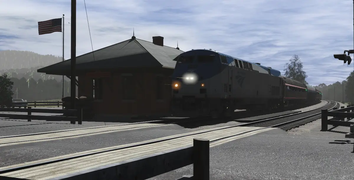 An Amtrak train approaches a station with an American flag flying, overlaid with the text 'i'm not lazy, i'm in…