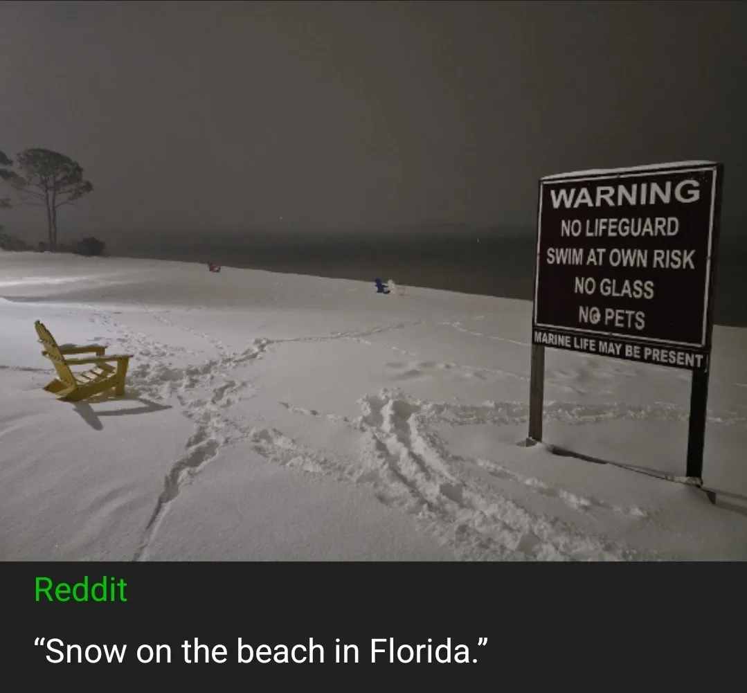 A snowy beach scene with a yellow Adirondack chair and footprints in the snow, next to a warning sign that reads 'WARNING NO…