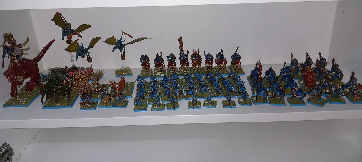 A white shelf displays a large collection of painted miniature figurines, mostly blue and red fantasy warriors and monsters…