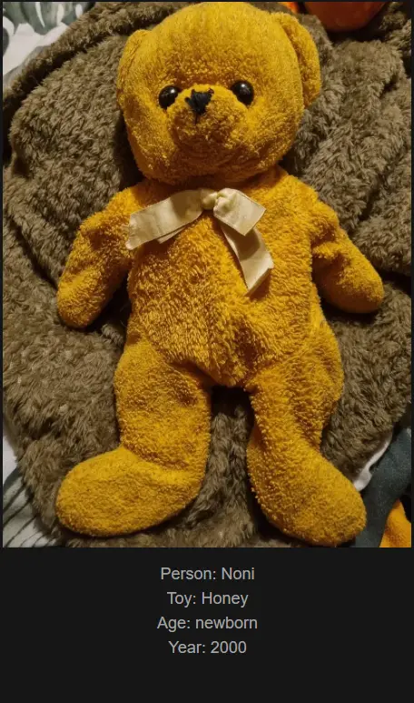 A yellow plush teddy bear with a beige bow lies on a brown fluffy blanket. Text overlaid at the bottom identifies it as…