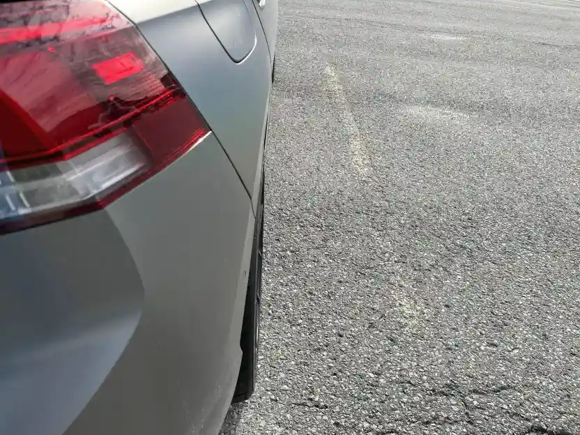 A close-up photo of the rear passenger side of a gray car parked on asphalt, showing the taillight, door handle, and wheel…