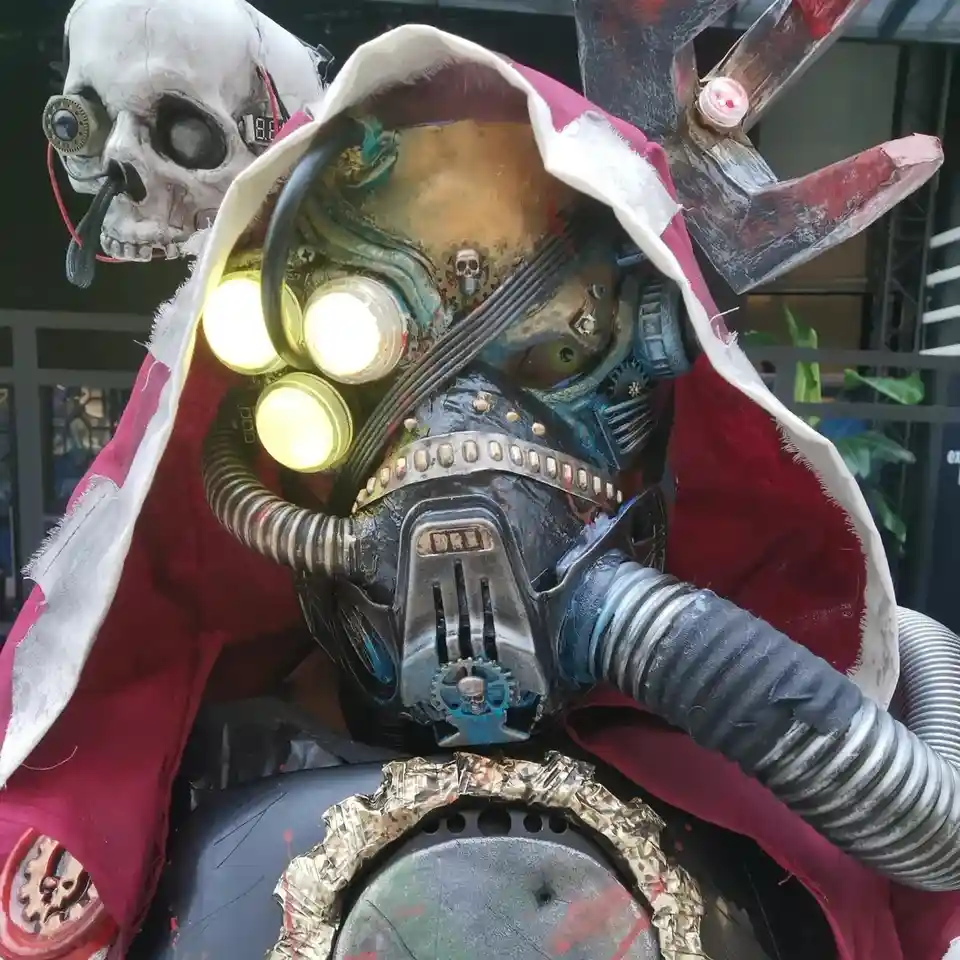 A person in a highly detailed, steampunk-inspired costume with a mechanical mask featuring glowing yellow lights, exposed…