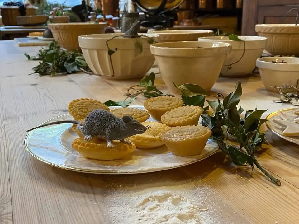 A small, gray plastic rat figurine is positioned on top of a plate holding several golden-brown, fluted pastries, likely…