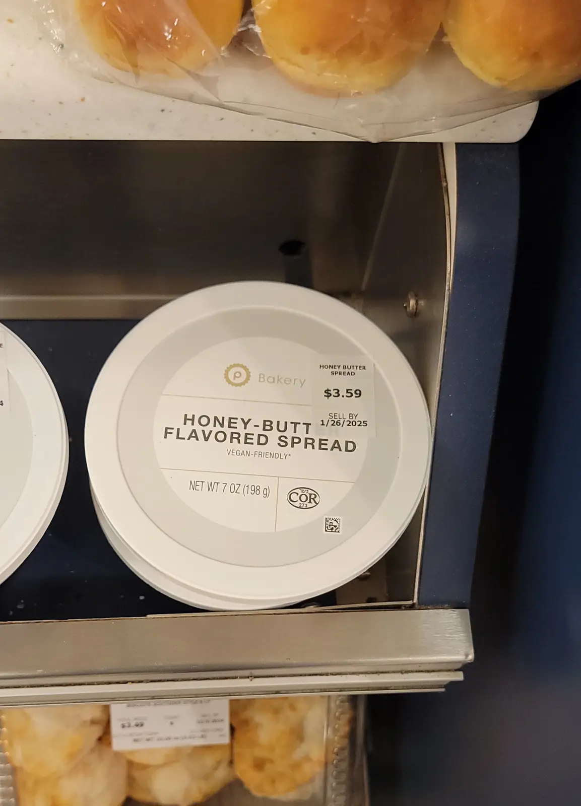A close-up of a white tub of 'Honey-Butt Flavored Spread' in a bakery section, priced at $3.59, with a 'sell by' date of…
