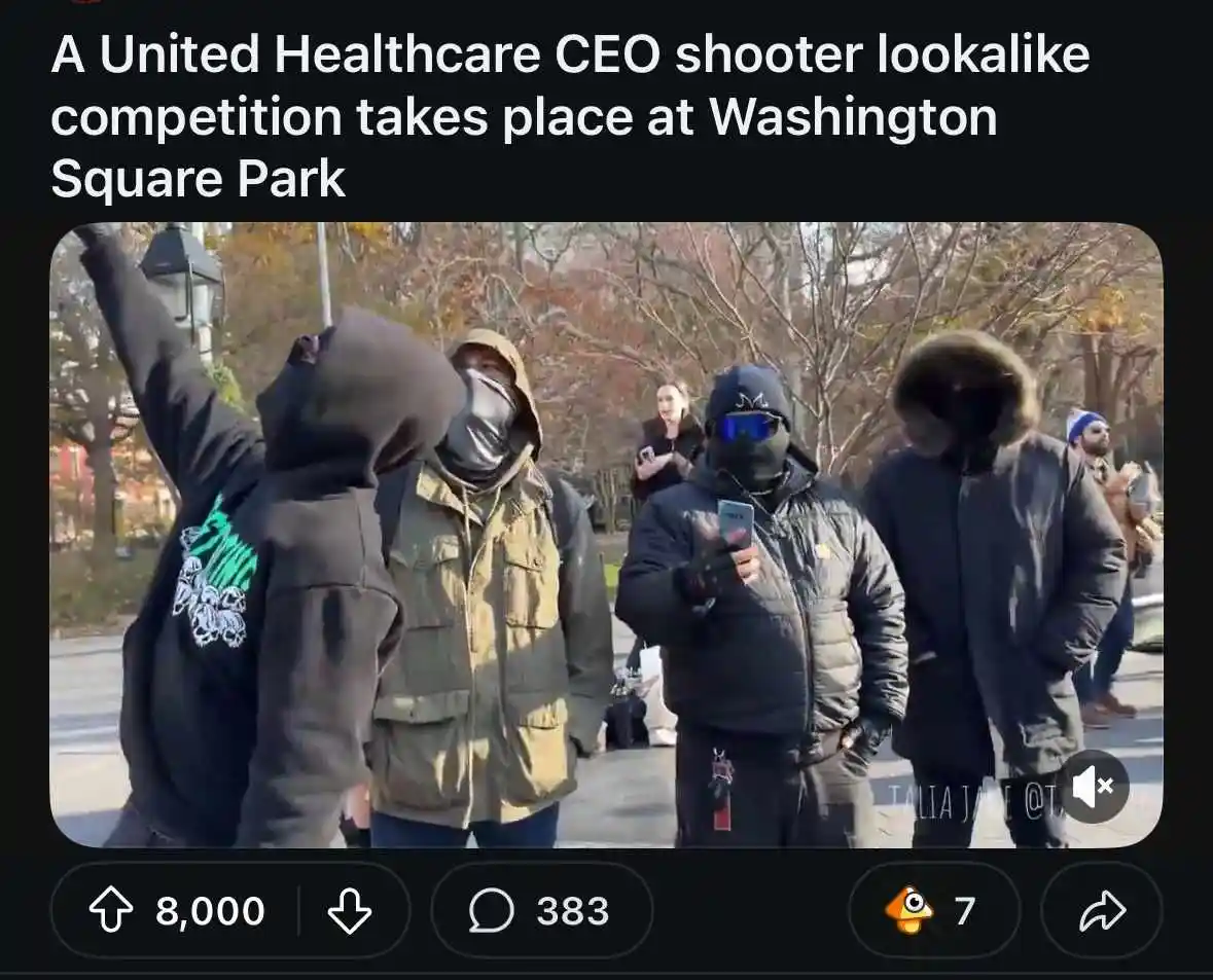 Several people dressed in dark, hooded, and masked winter clothing stand outdoors in a park, with one person raising an arm…