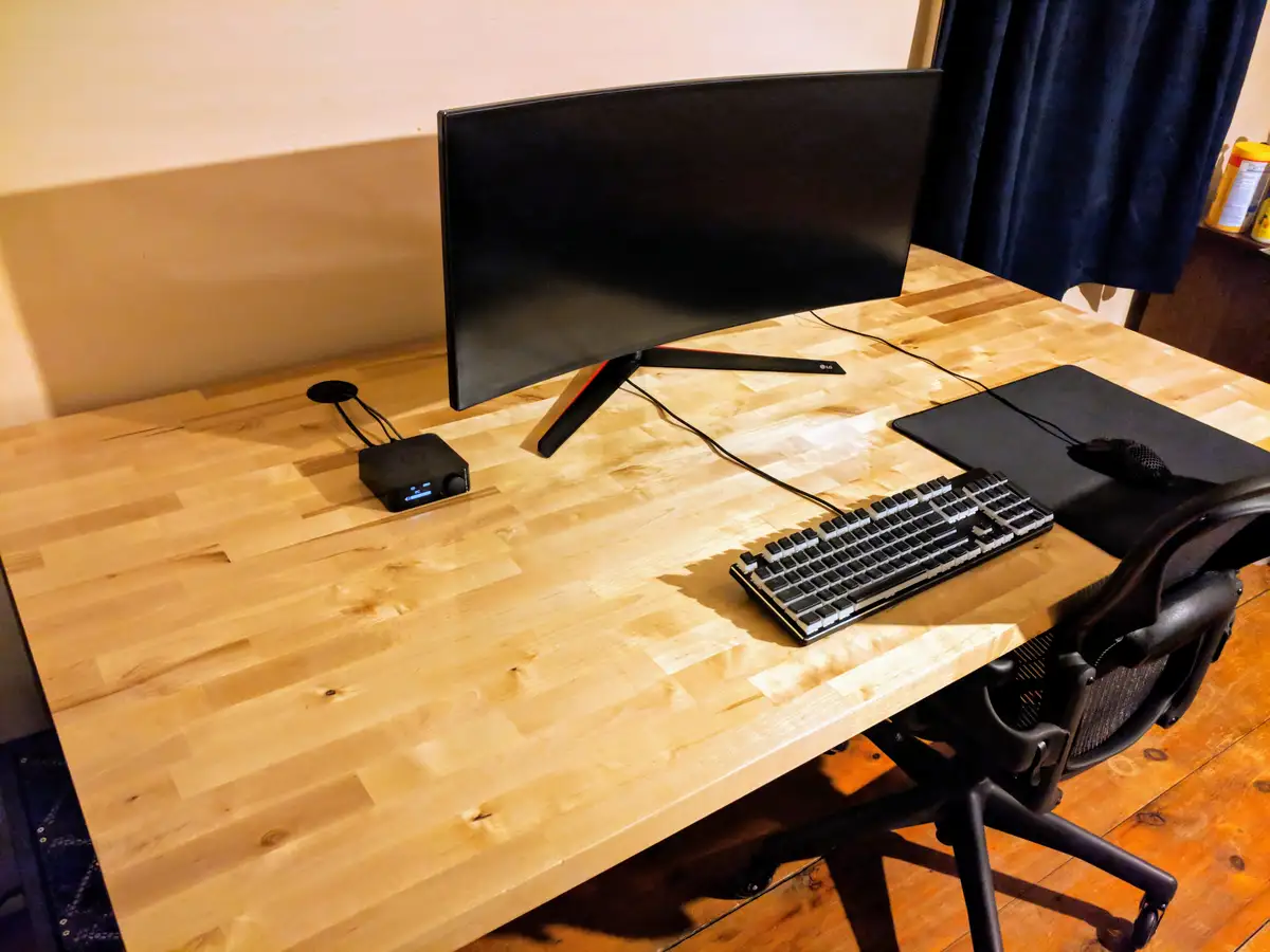A minimalist wooden desk setup with a curved LG monitor, a mechanical keyboard, a mouse on a large mousepad, and a small…