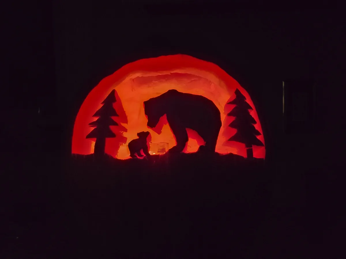 A carved ice sculpture illuminated from within by red light, depicting the silhouette of a large bear and a smaller bear cub…