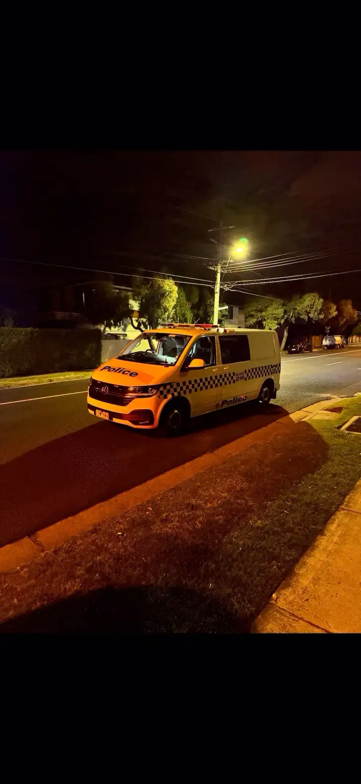 A yellow and white police van with checkered markings is parked on a residential street at night, illuminated by a…