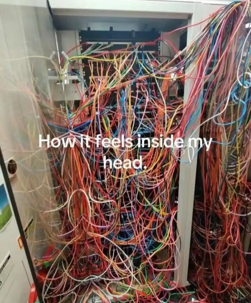 An open server rack filled with a chaotic tangle of multicolored wires and cables spilling out from the top and sides. White…