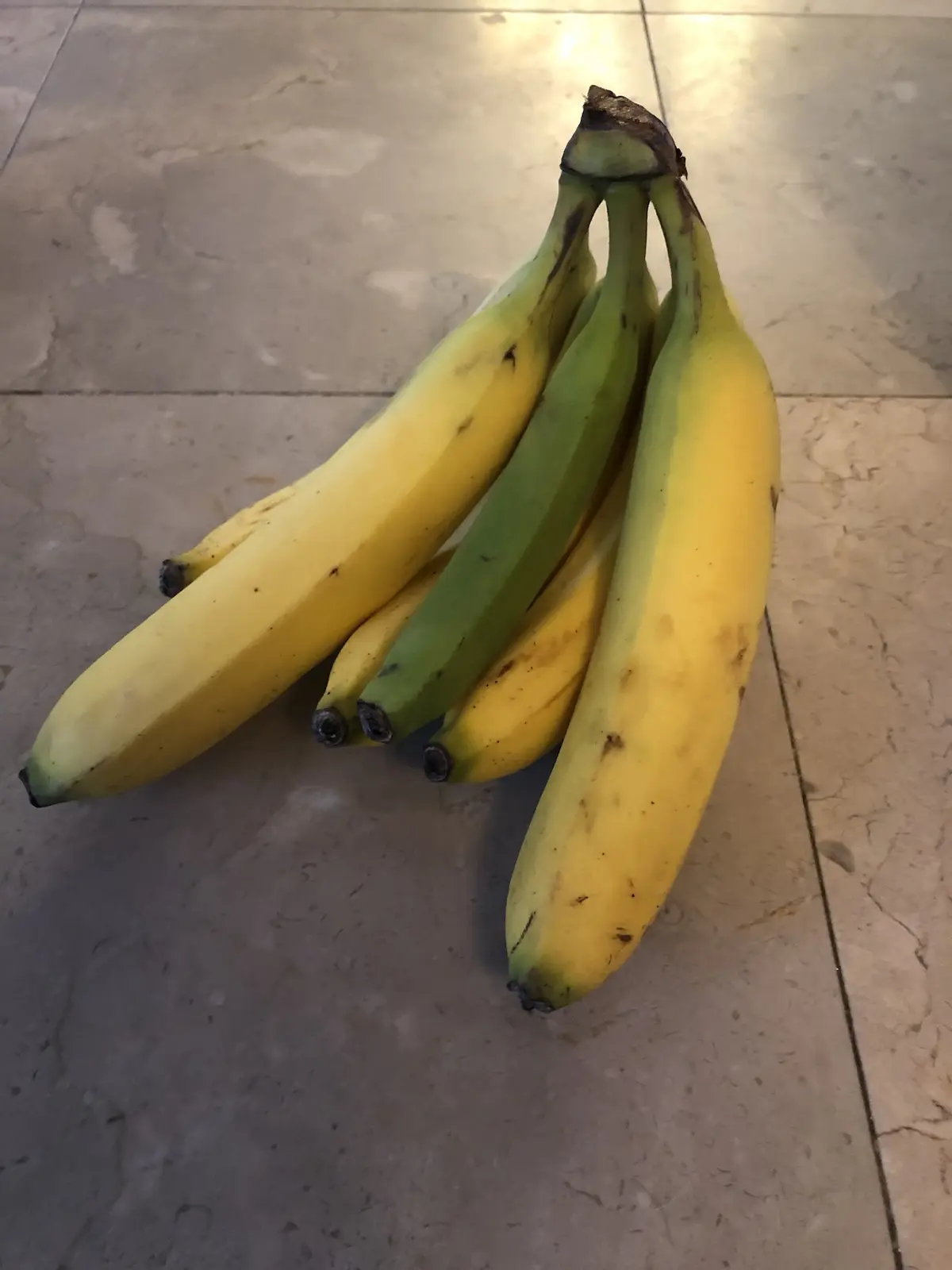 A bunch of bananas with varying ripeness, some yellow and some green, lying on a tiled floor. The overlaid text reads 'i'm…