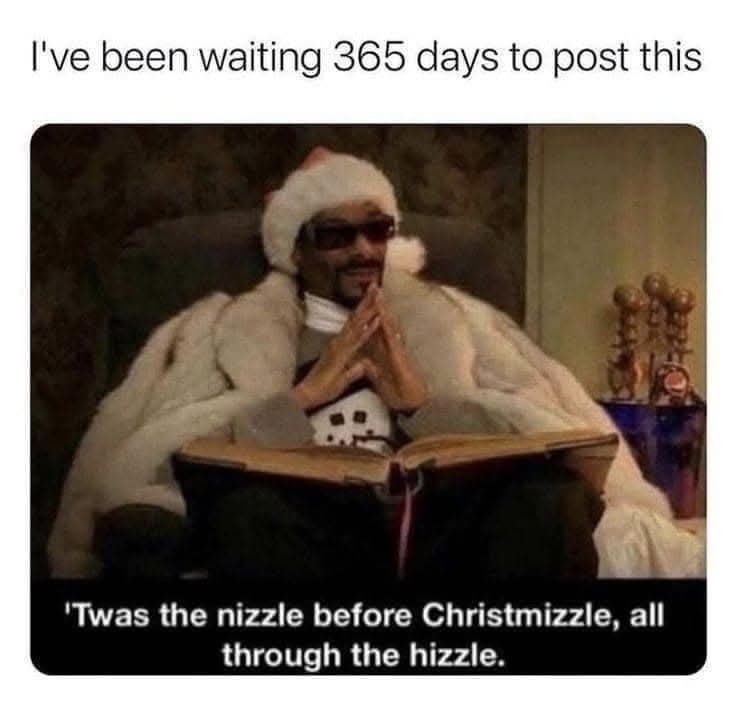 A man wearing a Santa hat and sunglasses sits in a chair, draped in a white fur coat, with his hands clasped as if in prayer…