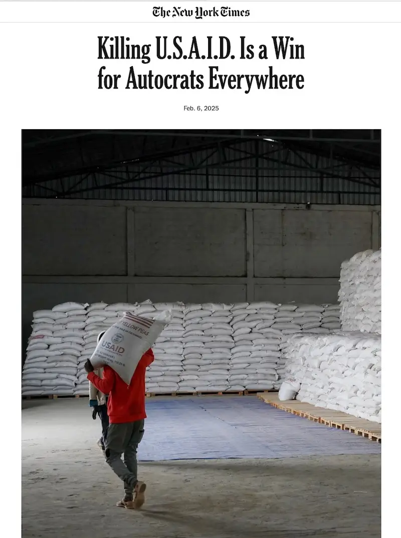 A person in a red shirt carries a large white sack labeled 'USAID' on their shoulder through a warehouse filled with stacks…