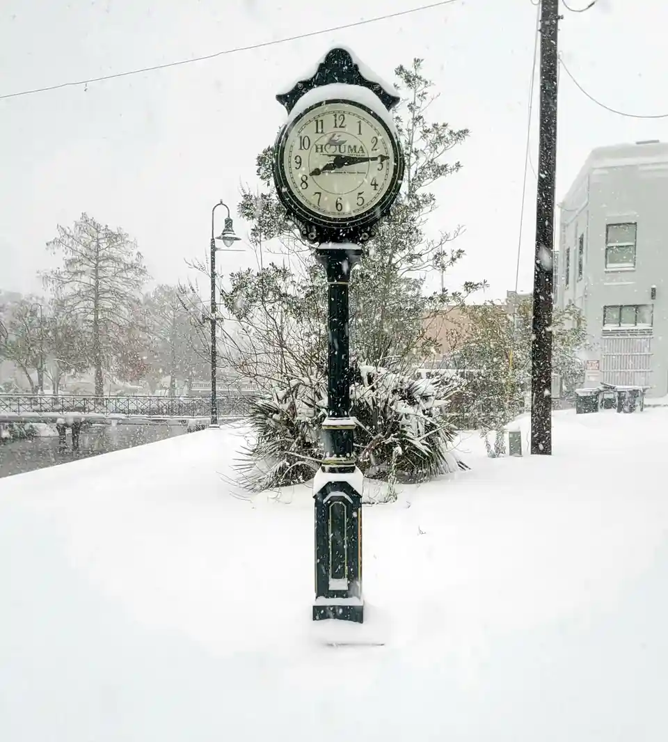 A black ornate street clock in Houma, Louisiana, is heavily covered in snow, with snow also blanketing the ground and…