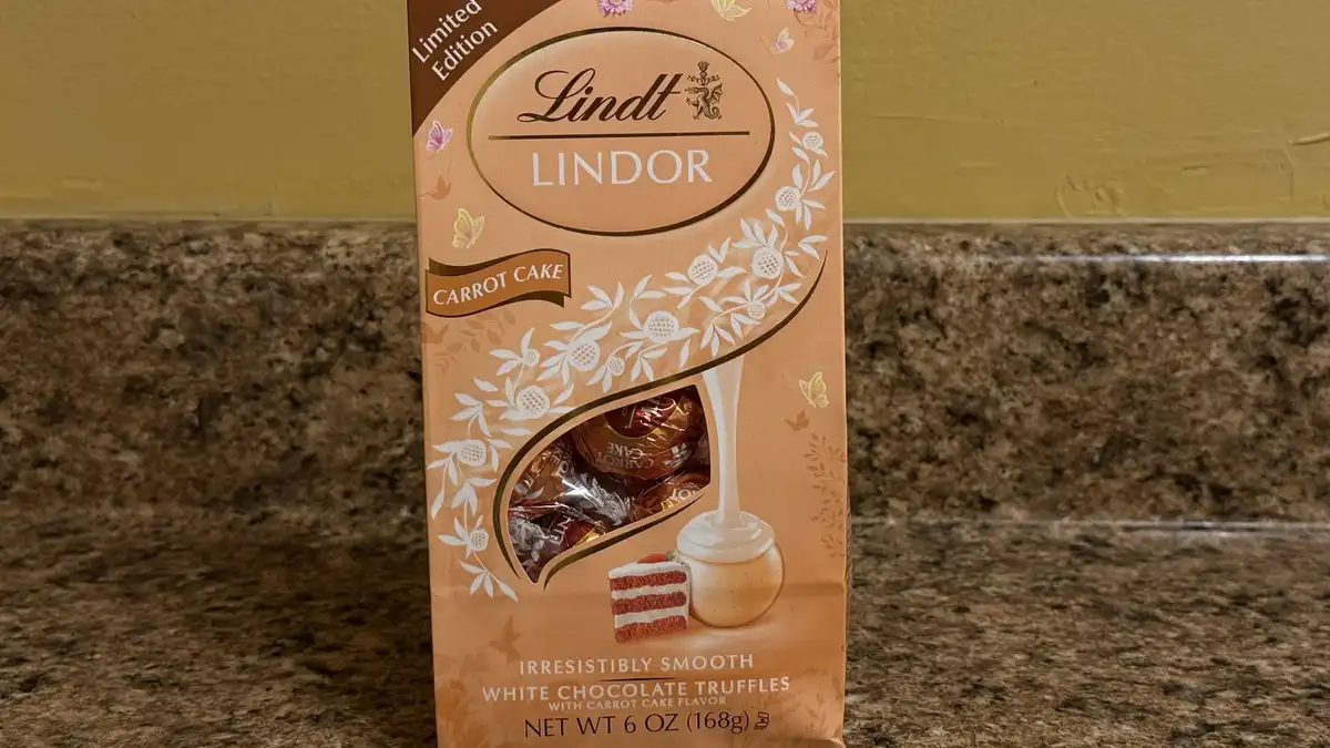 A close-up photo of a Lindt LINDOR limited edition white chocolate truffle box with carrot cake flavor, standing on a…